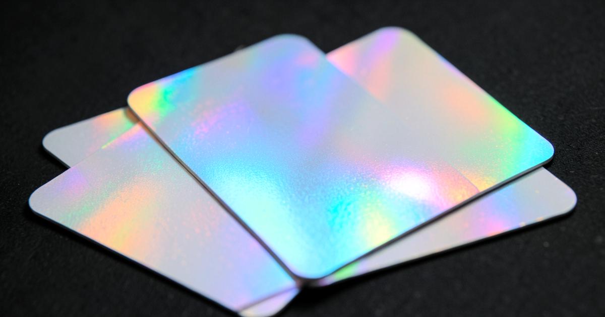 Blank holographic trading cards with rainbow foil shine fanned out on a dark surface